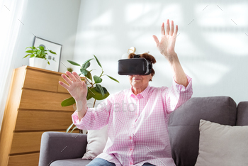 Senior woman wearing virtual reality goggles at home. Emotional lady with virtual headset or 3d