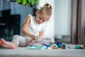 Little girl playing with small constructor toy on floor in home, educational game, spending leisure