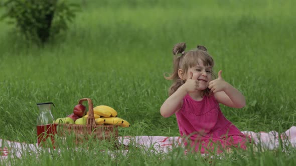 Weekend at Picnic. Lovely Caucasian Child Girl on Green Grass Meadow Sit on Blanket Show Thumbs Up