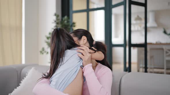 Happy Brunette Mother Hugs Running Daughter Sitting on Couch