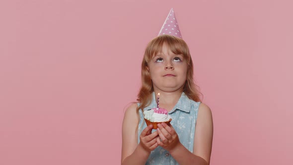 Happy Child Girl Kid Celebrating Birthday Party Makes Wish Blowing Burning Candle on Small Cupcake