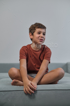 A boy sits, cross-legged, tongue out in jest. His playful pose counters the structured routines many