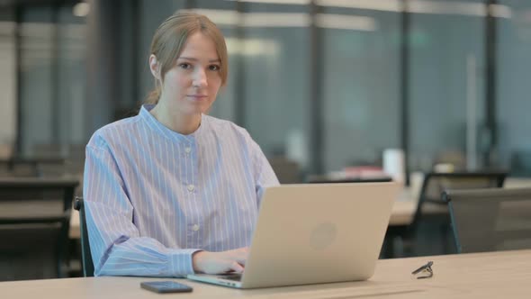 Young Woman Smiling at Camera While Using Laptop in Office