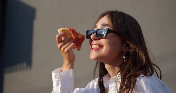 girl in sunglasses is eating slice of pizza. girl bites pizza, smiles and dances