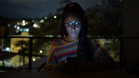 Black woman browsing smartphone in city at night