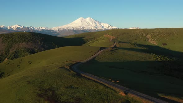 Top view of green field, winding roads and Caucasus mountains.Sunrise above Mount Elbrus