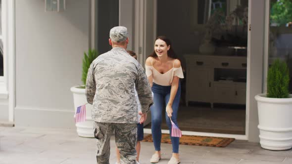 Happy caucasian male soldier lifting son and greeting wife outside their house