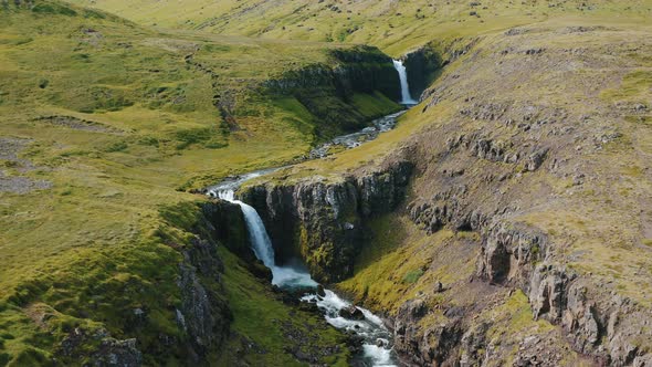 Drone Flight Over a Waterfall Descending in the Middle of the Green Hills in Iceland Summertime