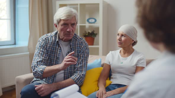 Female Doctor Visiting Aged Woman with Cancer Sitting on Couch with Husband