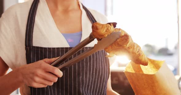 Waitress packing croissants in paper bag at caf������������