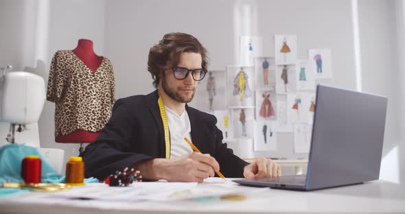 Male Fashion Designer Look at Laptop Working with Sketches in Studio Atelier