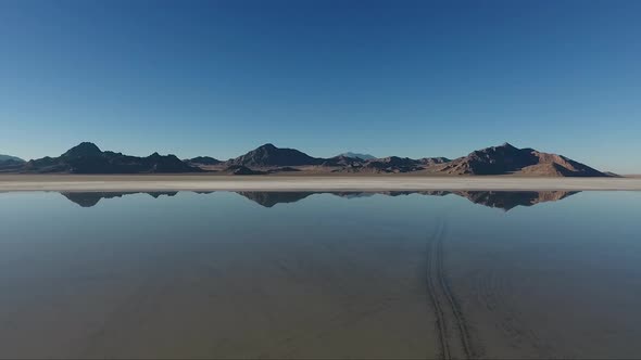 An aerial drone shot of smooth water covering the Bonneville Salt Flats reflects distant mountains.