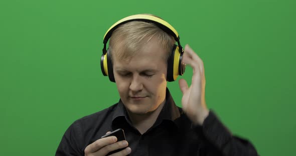 Guy Listens To Music in Wireless Yellow Headphones and Dances. Green Screen