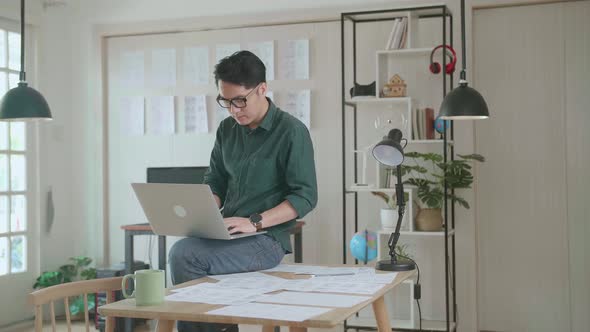 Creative Designer Sits On His Desk Holds Laptop On The Knees And Working On The Project