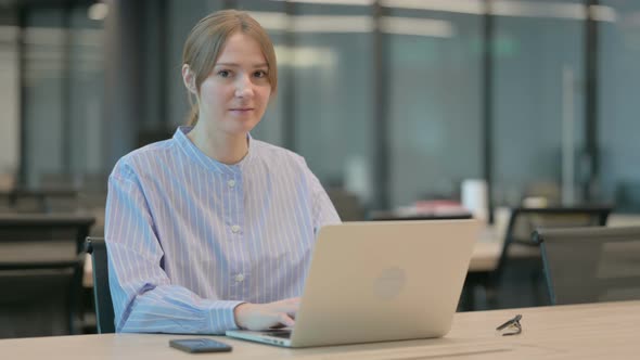 Young Woman Showing Thumbs Up Sign While Using Laptop in Office