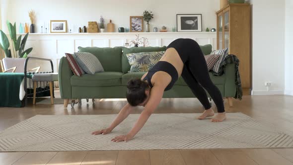 Indian Woman moving into downward facing dog pose while practicing yoga in home