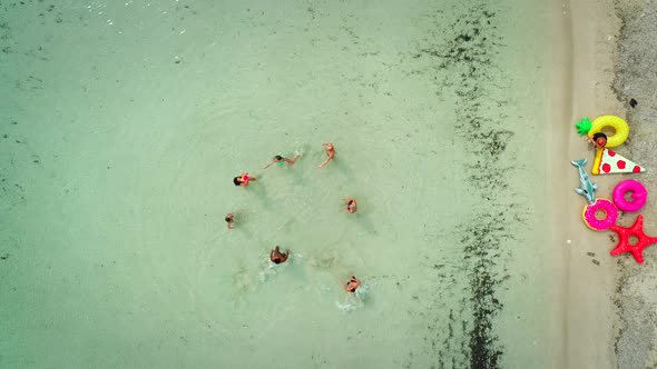 Aerial view of friends playing volleyball standing in sea by sandy beach.