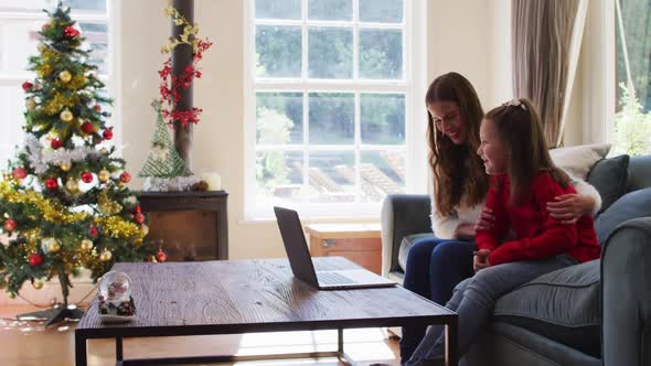 Caucasian mother and daughter smiling and waving while having a video call on laptop sitting on the