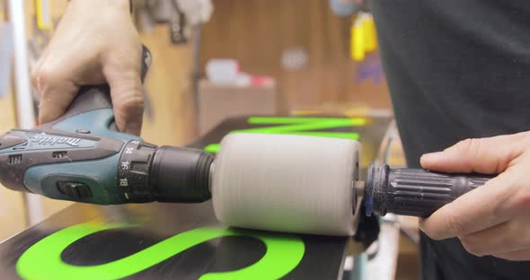 Repairman Start Polishing A Waxed Snowboard. Motion Toward And Backward