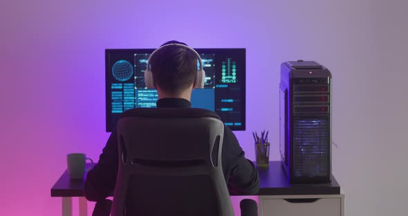 Man Programmer in Headphones Working at a Computer in Data Center at Night