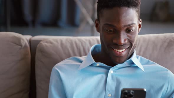 Smiling young male sending messages using smartphone on the couch