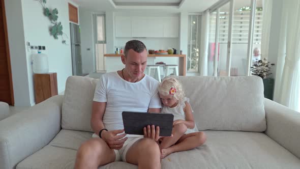 Father and His Daughter Sitting on the Couch and Using a Tablet