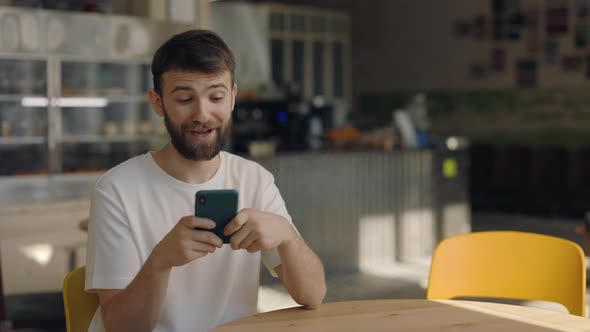 Cheerful Bearded Man Surfing Internet on Cell Phone at Cafe