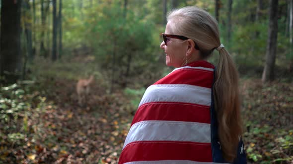 Closeup of woman looking to the left and walking through a forest with a flag wrapped around her.