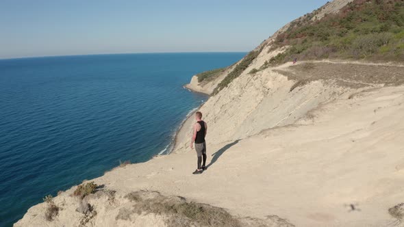 Aerial View of Man Stands on Top of Mountain Near Cliff, Beautiful View of Sea