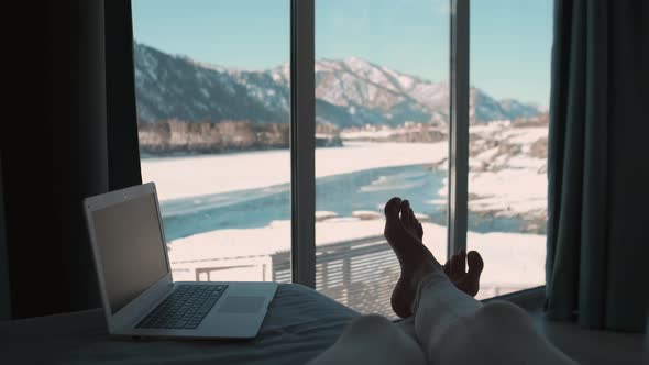 A Female Freelancer Lies on a Bed Next to a Laptop and Looks Out the Window While on Vacation