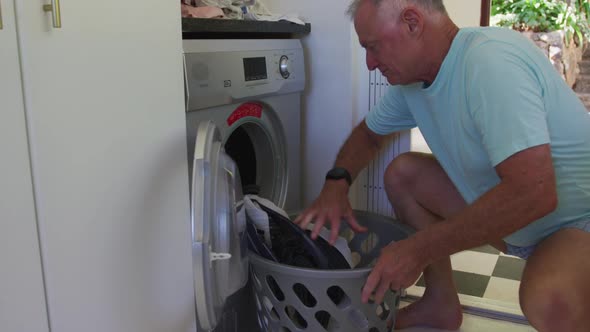 Caucasian senior man putting clothes in washing machine at home