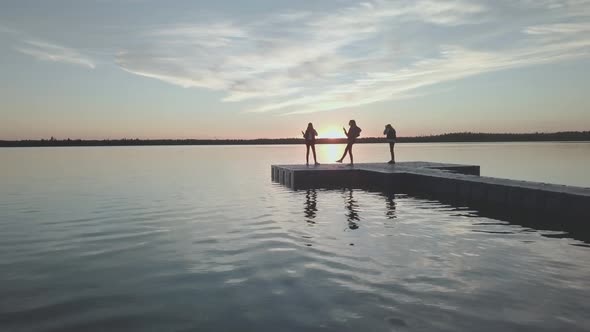 Young girls stand on the pier on the sunset.