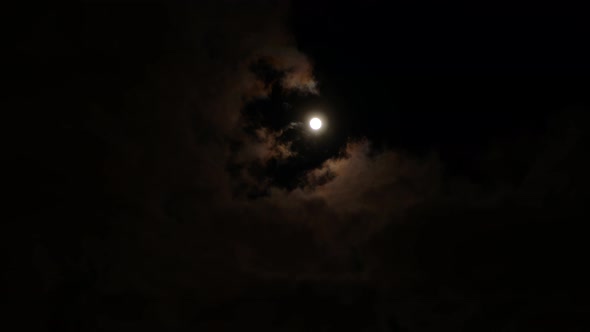 Clouds are drifting across the sky and changing their color on the background of glowing full moon