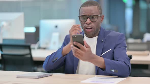 African Businessman Reacting to Loss on Smartphone in Office