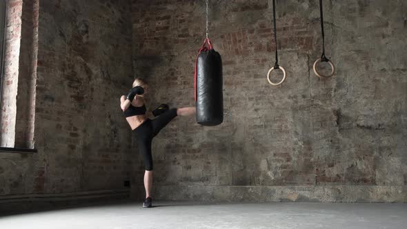 Girl punches and kicks the punches bag in gym. Woman punches and kicks the punches bag