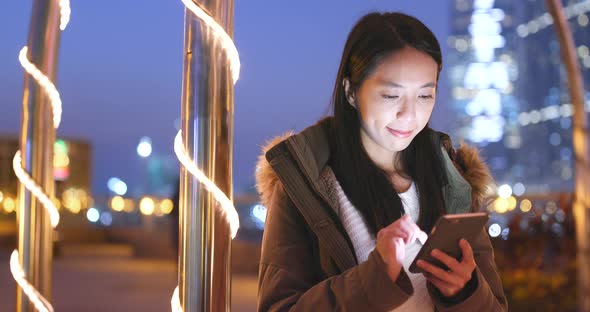 Woman sending sms on smart phone in city at night with city building background