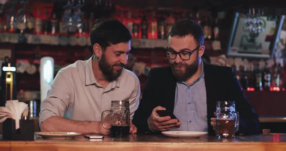 Two Old Friends with Smartphone Talking in the Beer Pub at Night.