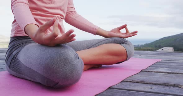 Low section of caucasian woman meditating in lotus position on deck on rural mountainside