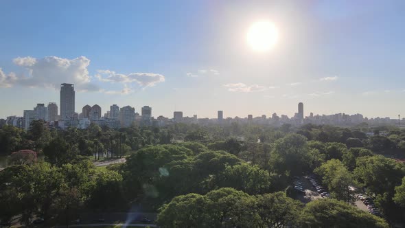 Aerial dolly in flying over Palermo Woods with buildings in background at daytime, Buenos Aires