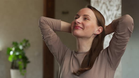 Cheerful Young Beautiful Woman Holding Her Hands Behind Her Head and Smiling While Sitting at Her