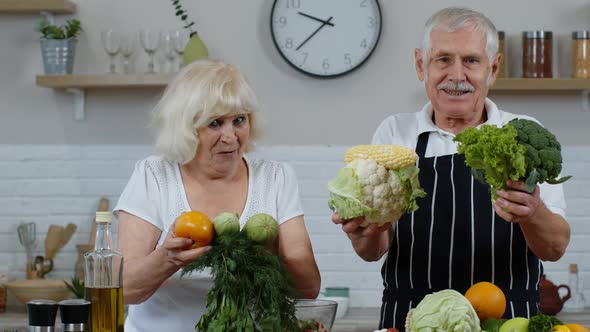 Senior Grandparents Couple in Kitchen. Mature Man and Woman Recommending Eating Raw Vegetable Food