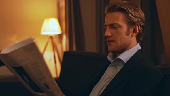 Confident Successful Young Businessman in Suit Sitting in the Evening Reading Newspaper in