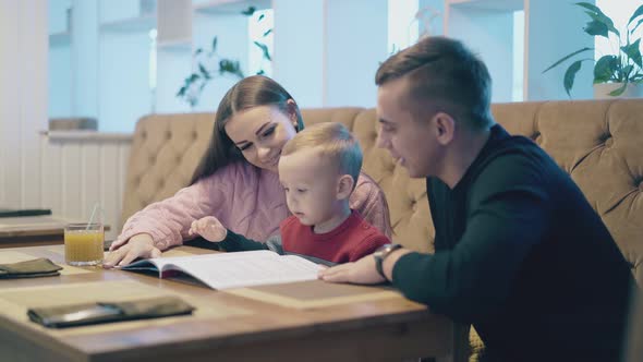 Boy Kid Sits Between Mother and Father in Restaurant