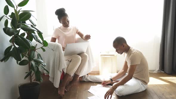 Man Sits on the Floor with Papers While His Wife Work on Laptop