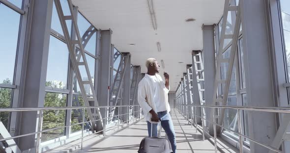 Active Afro American Guy Foreign Student Wears White Shirt, Dances at Airport with Luggage Suitcase