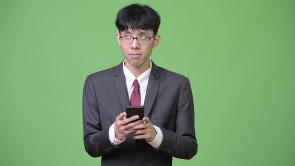 Young Asian Businessman Thinking While Using Phone