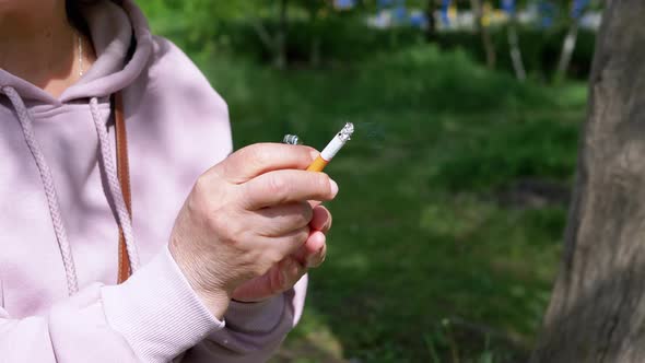 Woman Holding a Cigarette and a Lighter in Hands Sitting in Nature on Sun