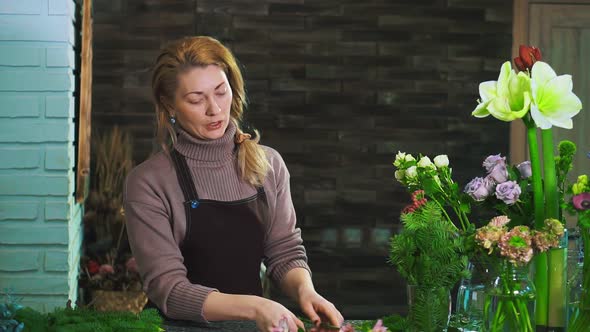 A Woman Florist in an Apron, Standing on the Counter in a Flower Shop, Preparing a Bouquet of