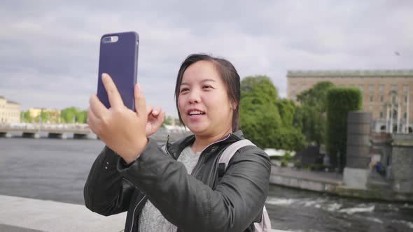 Happy Asian woman having video call on smartphone on small street by the river in Sweden