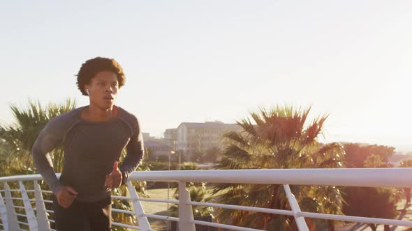 Fit african american man exercising outdoors in city wearing earphones, running on footbridge